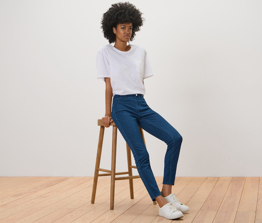 Frau sitzt auf einem Hocker und trägt Jeggings.