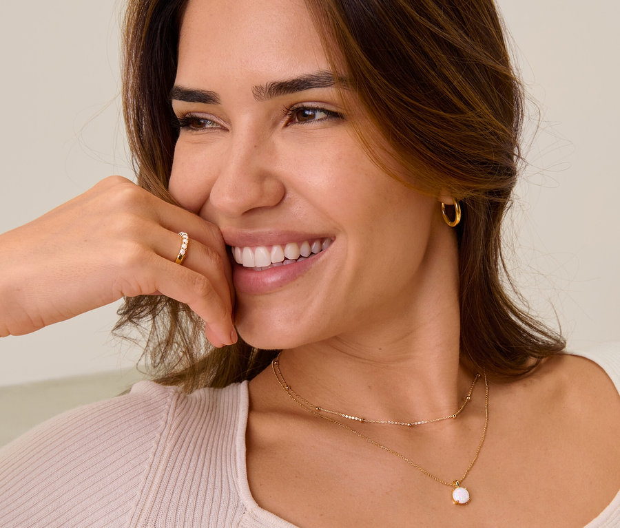 Lächelnde Frau mit goldfarbenem Creolen-Set, einem 925 Silber Ring mit synthetischen Opalen, einer 925 Silber Kette mit synthetischem Opal und einer 375 Gold Kette Kugeln.