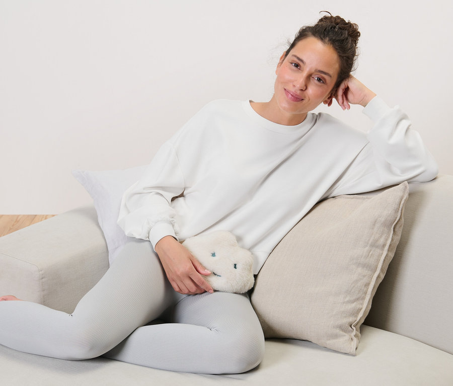 Frau sitzt auf Couch und hält Kirschkern-Wärmekissen in Wolkenform.