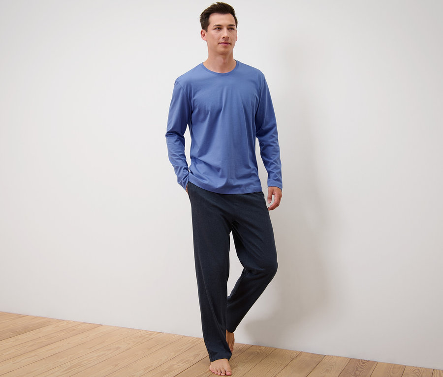 Mann steht und trägt einen blau-dunkelblauen Pyjama.