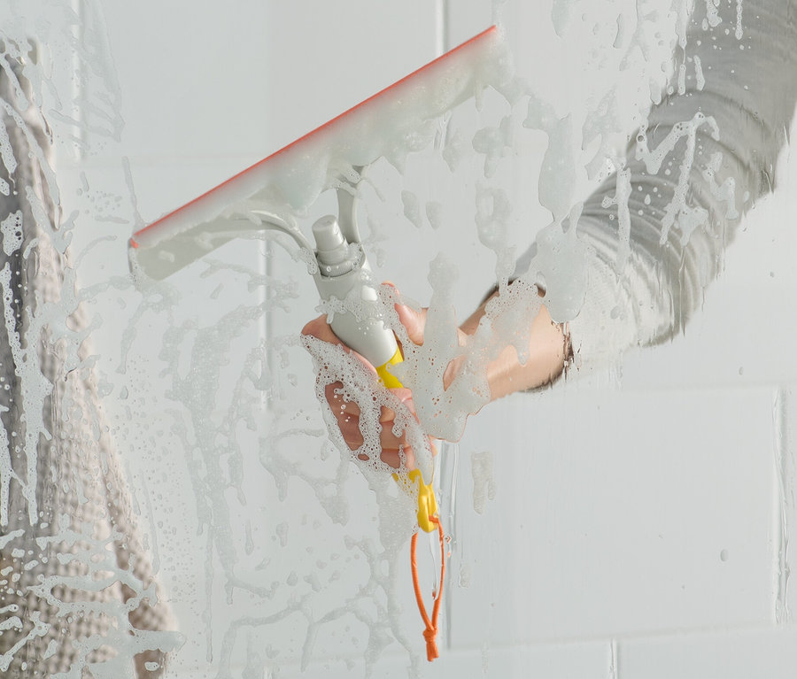 Frau wischt mit einem 3-in-1-Fensterwischer eine gläserne Duschwand ab.