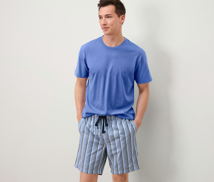 Mann trägt einen Shorty-Pyjama mit blauem T-Shirt und gestreiften Shorts.