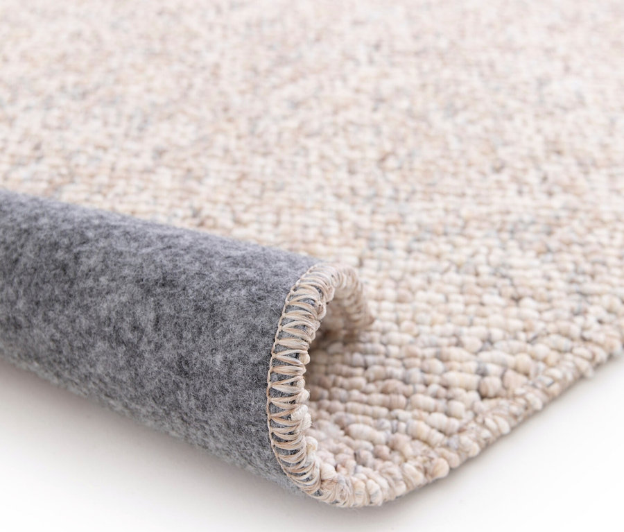 Detailansicht eines beigen Teppichs »Lino«, der auf einem weißen Hintergrund aufgerollt ist.