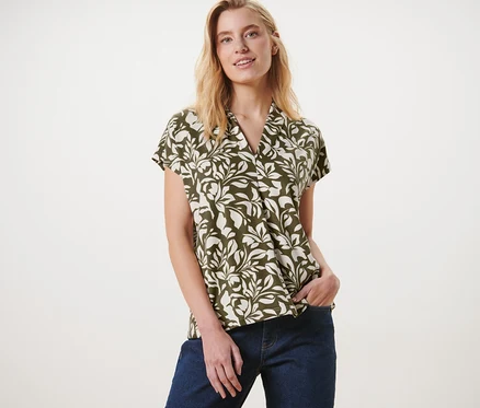Frau posiert in einem bedruckten Blusenshirt mit V-Ausschnitt und Jeans.