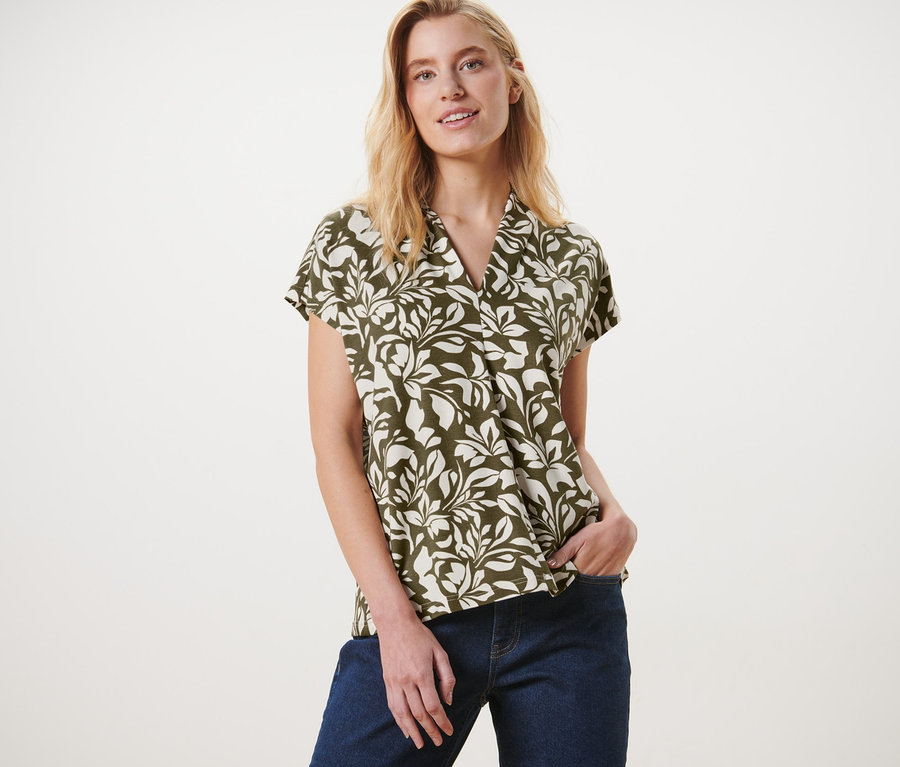 Frau posiert in einem bedruckten Blusenshirt mit V-Ausschnitt und Jeans.