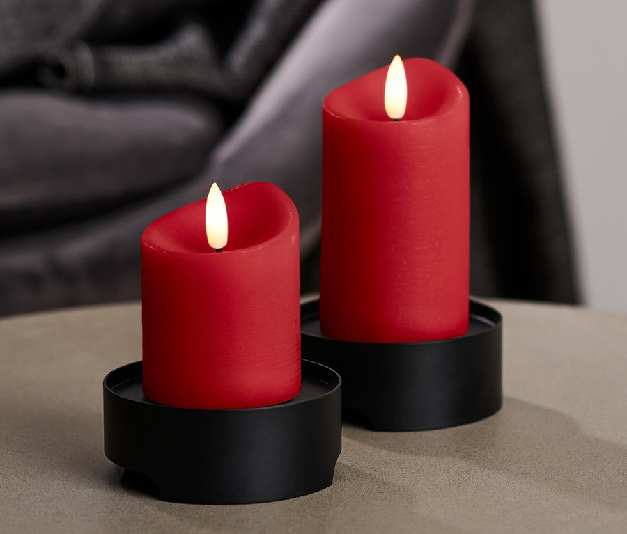 Zwei rote LED-Echtwachskerzen auf schwarzen Haltern stehen auf einem Tisch.