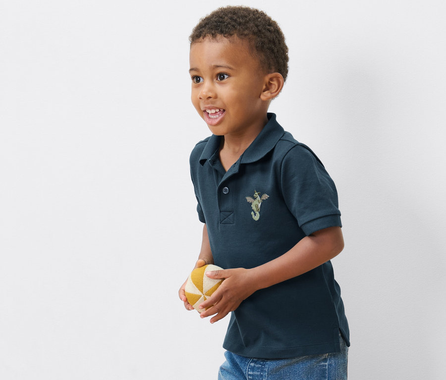 Junge trägt eines von 2 Kinder-Poloshirts aus Baumwoll-Piqué und hält einen Ball.