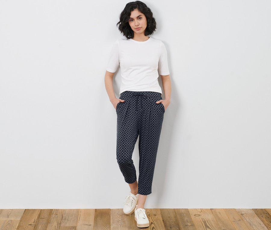Frau posiert in einem weißen T-Shirt und einer bedruckten 3/4-Jerseyhose.