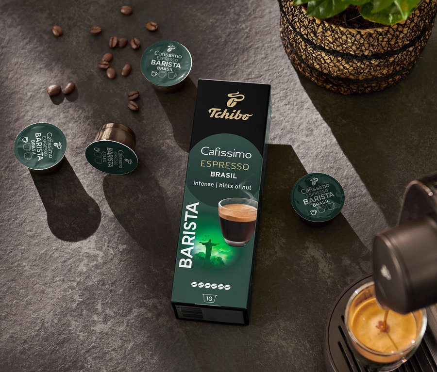 Espressomaschine füllt Tasse. Im Hintergrund Packung Cafissimo BARISTA Espresso Brasil - 10 Kapseln und Kaffeebohne.