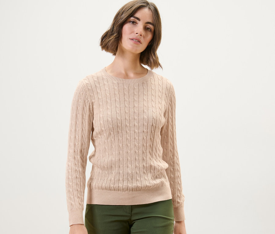 Frau trägt einen cremefarbenen Zopfstrickpullover.