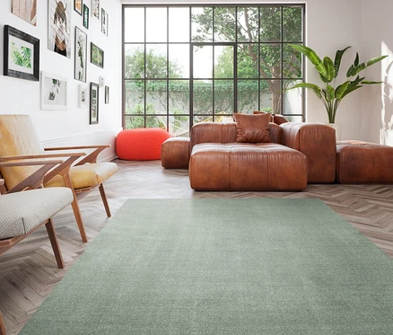 Wohnzimmer mit braunem Ledersofa, orangefarbenem Hocker und grünem Teppich »Mellow«.