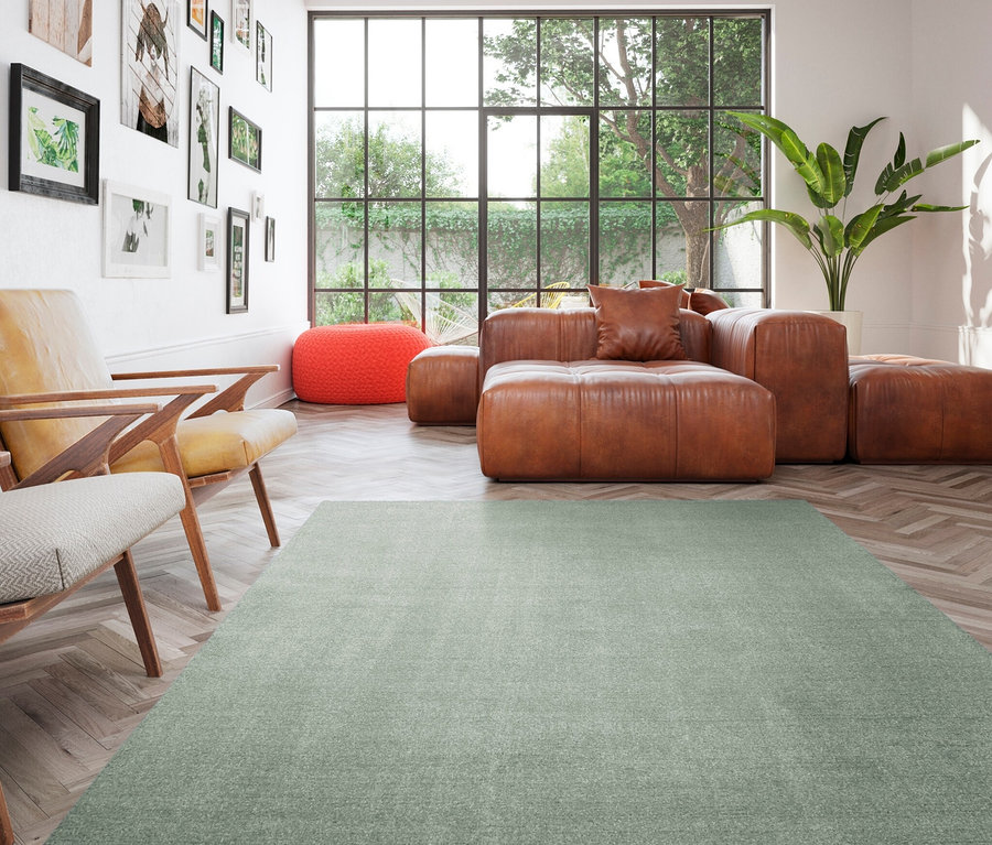 Wohnzimmer mit braunem Ledersofa, orangefarbenem Hocker und grünem Teppich »Mellow«.