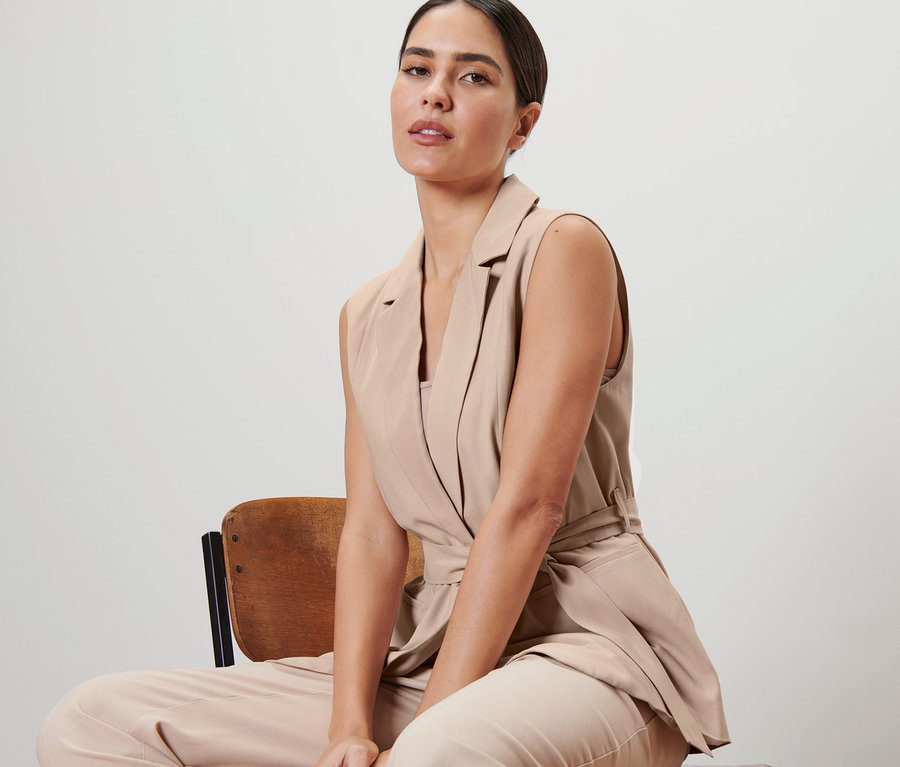 Frau sitzt auf einem Stuhl und trägt eine Weste mit Bindegürtel.