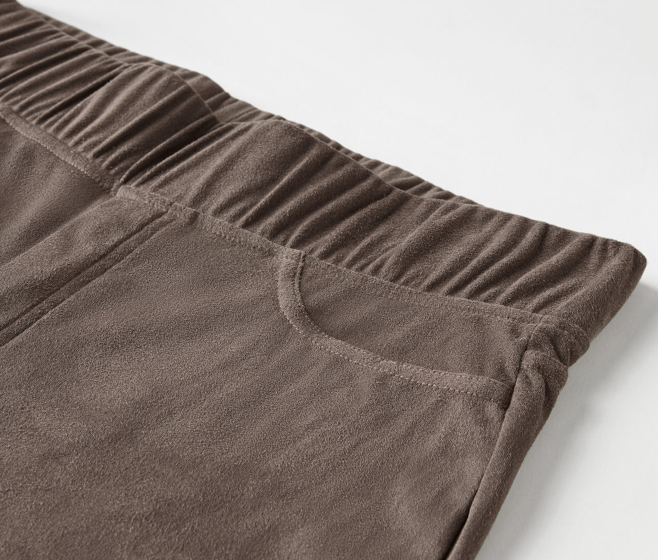 Detail einer braunen Hose mit Gummibund und Tasche.