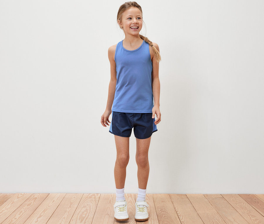 Lächelndes Mädchen steht und trägt ein blaues Sporttop und Sportshorts.