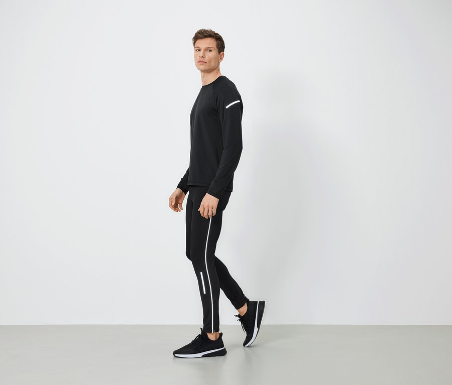 Mann in schwarzer Sportbekleidung mit reflektierenden Details geht auf grauem Boden.