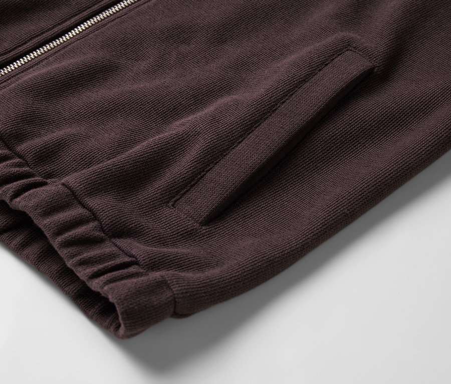 Detailaufnahme einer burgunderroten Sweatshirtjacke mit Reißverschluss, Tasche und Rippbündchen.