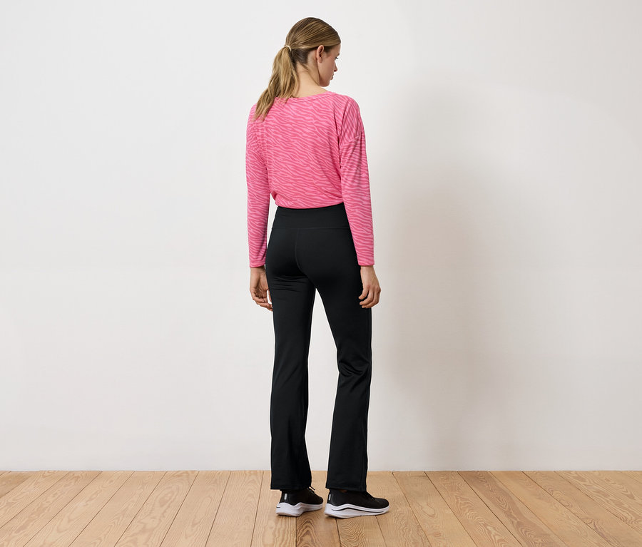 Frau mit dem Rücken zur Kamera trägt ein rosafarbenes Langarmshirt und eine schwarze Hose.