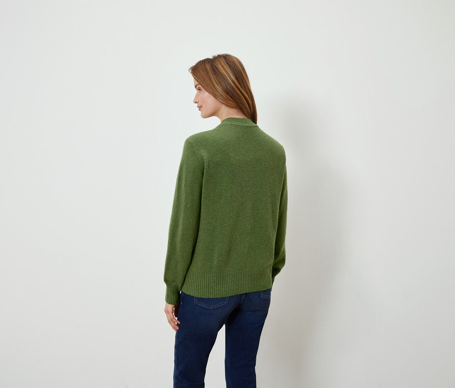 Frau blickt über die Schulter und trägt einen grünen Pullover und Jeans.