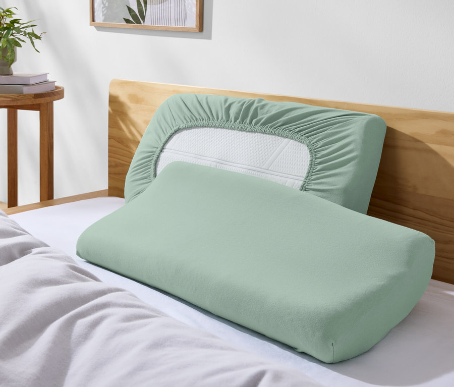 Zwei grüne Kissen auf einem Bett mit weißer Bettwäsche.