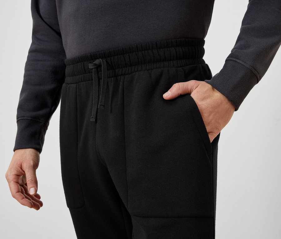 Mann mit Hand in der Tasche einer schwarzen Trainingshose.