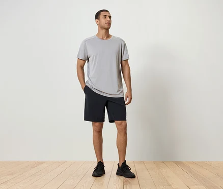 Mann steht mit der Hand in der Tasche der schwarzen Shorts, trägt ein graues T-Shirt und schwarze Schuhe.