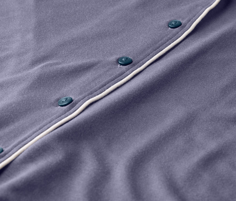 Detailaufnahme eines lila Pyjamas mit Knöpfen und weißer Paspelierung.