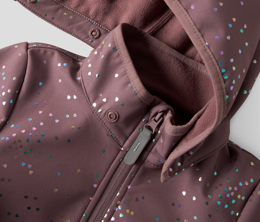 Nahaufnahme einer lila Softshelljacke mit Kapuze und Reißverschluss, verziert mit bunten Herzpunkten.