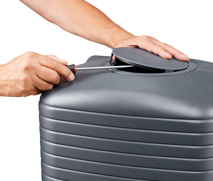 Eine Person schraubt mit einem Schraubenzieher an einem grauen, gerippten Tank, dessen Deckel teilweise geöffnet ist.