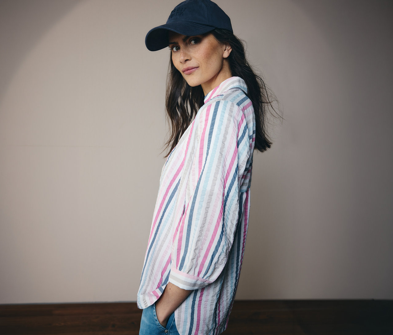 Frau mit blauem Hut und gestreifter CECIL Hemdbluse, die in die Kamera blickt.