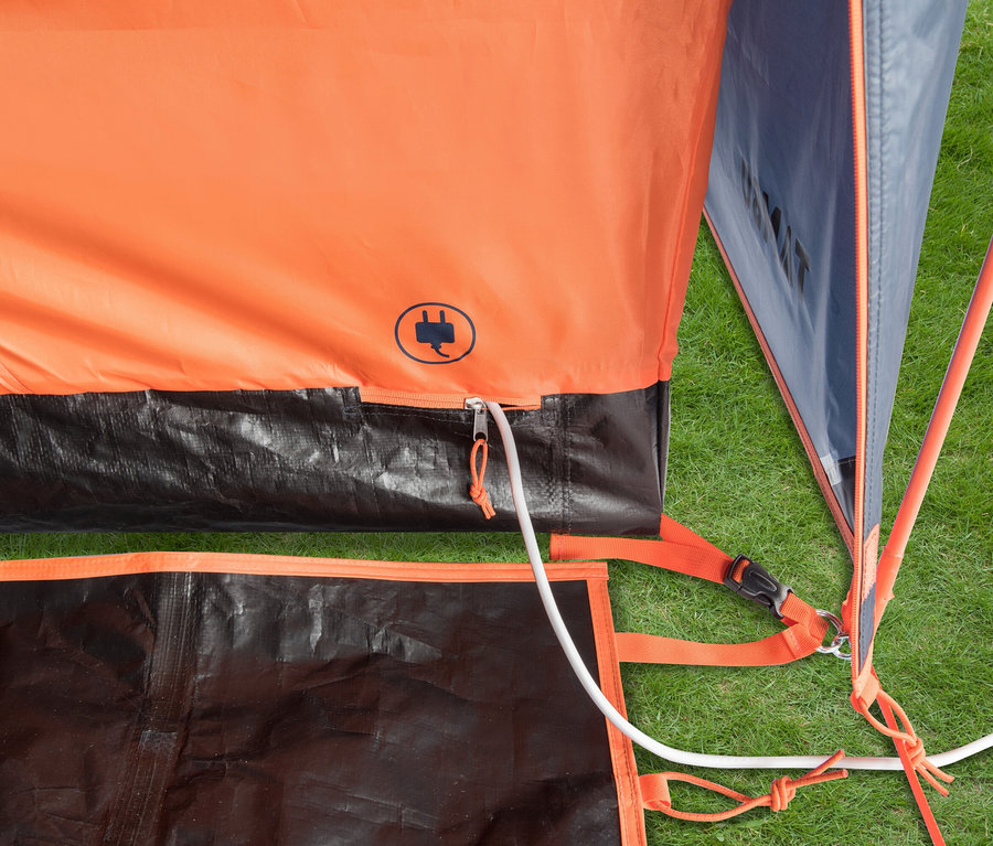 Nahaufnahme eines orangefarbenen Zeltes mit schwarzem Boden und weißem Kabel auf einer Wiese.