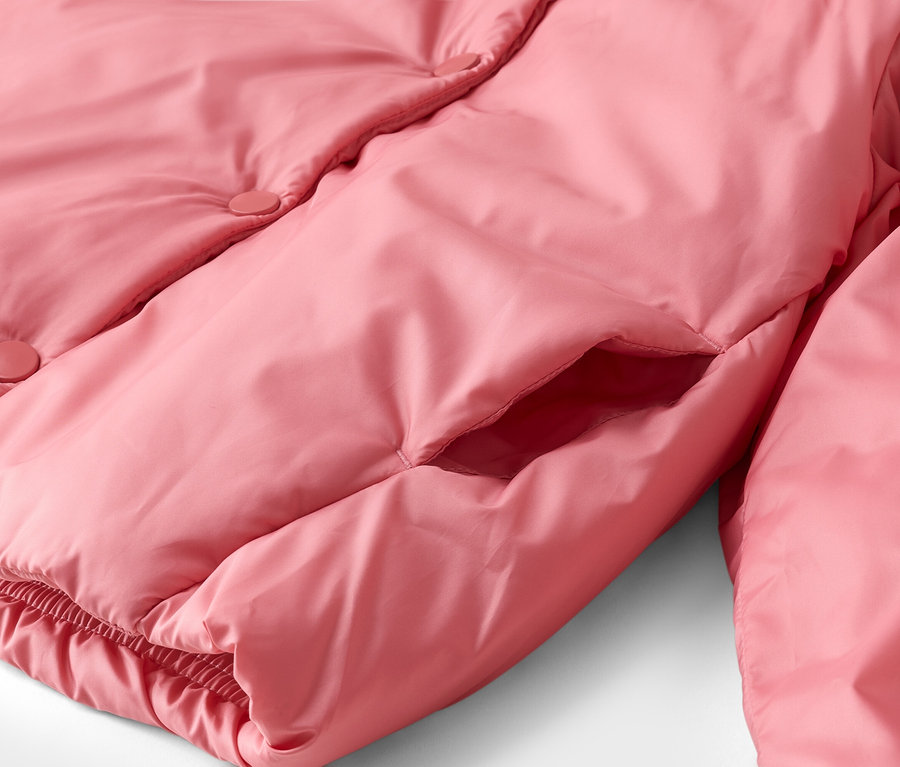 Nahaufnahme einer rosafarbenen Steppjacke mit Druckknöpfen, einer Eingrifftasche und einem gerafften Saum.