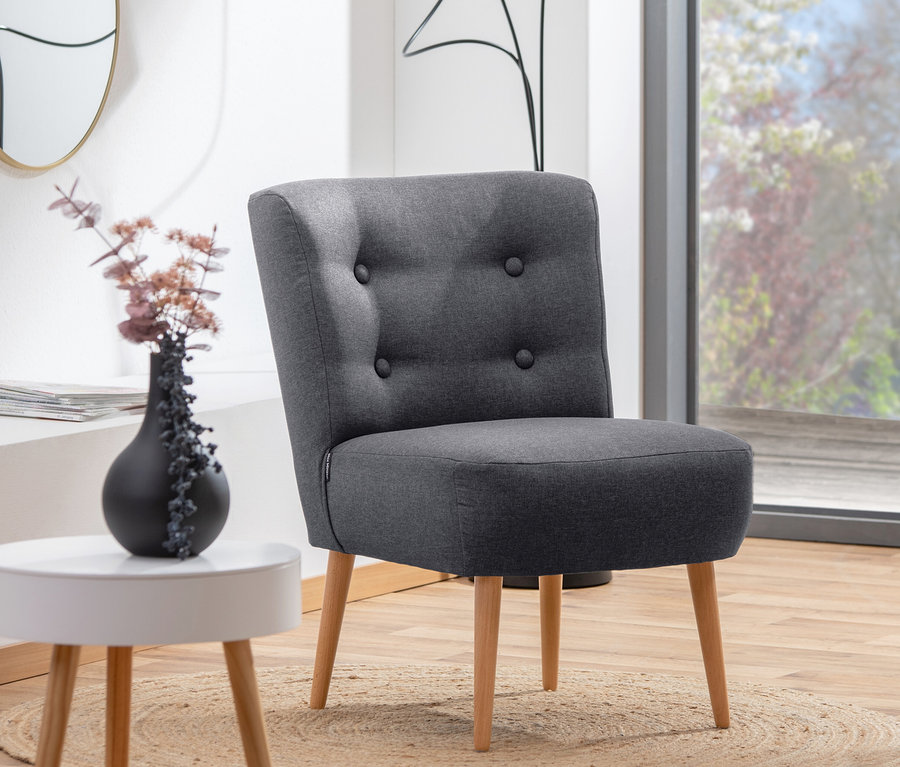 Der graphitfarbene Cocktail-Sessel »Fiona« steht auf einem runden Teppich vor einem Fenster.