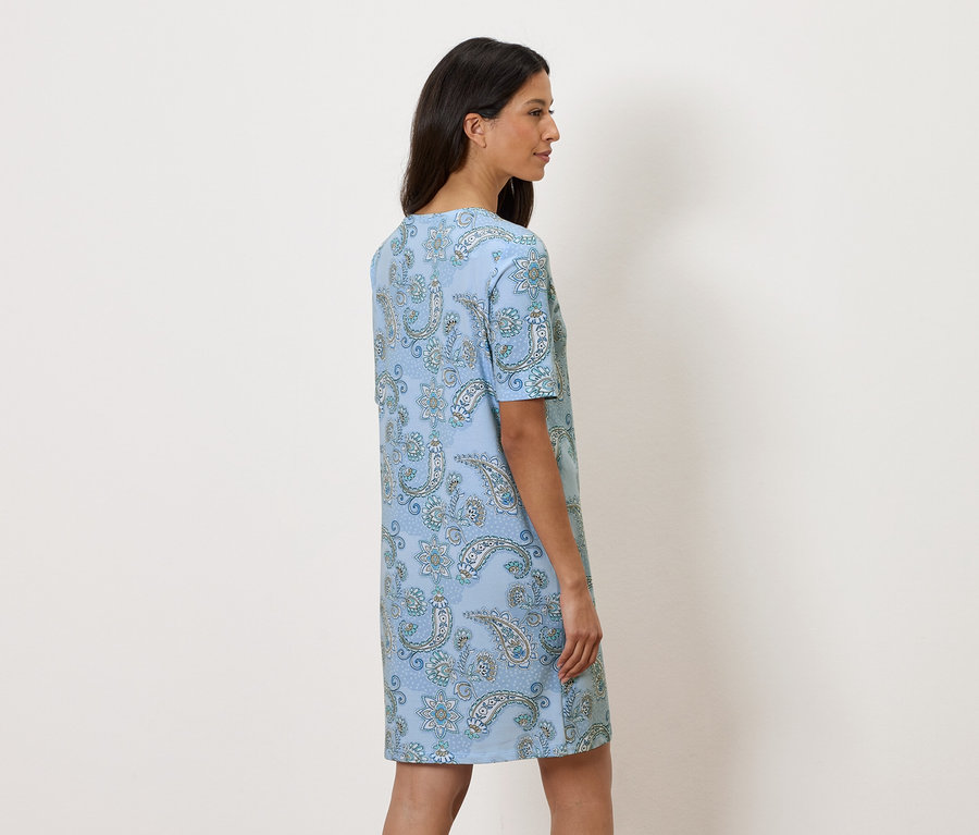 Frau steht seitlich und trägt ein hellblaues Kleid mit Paisley-Muster.