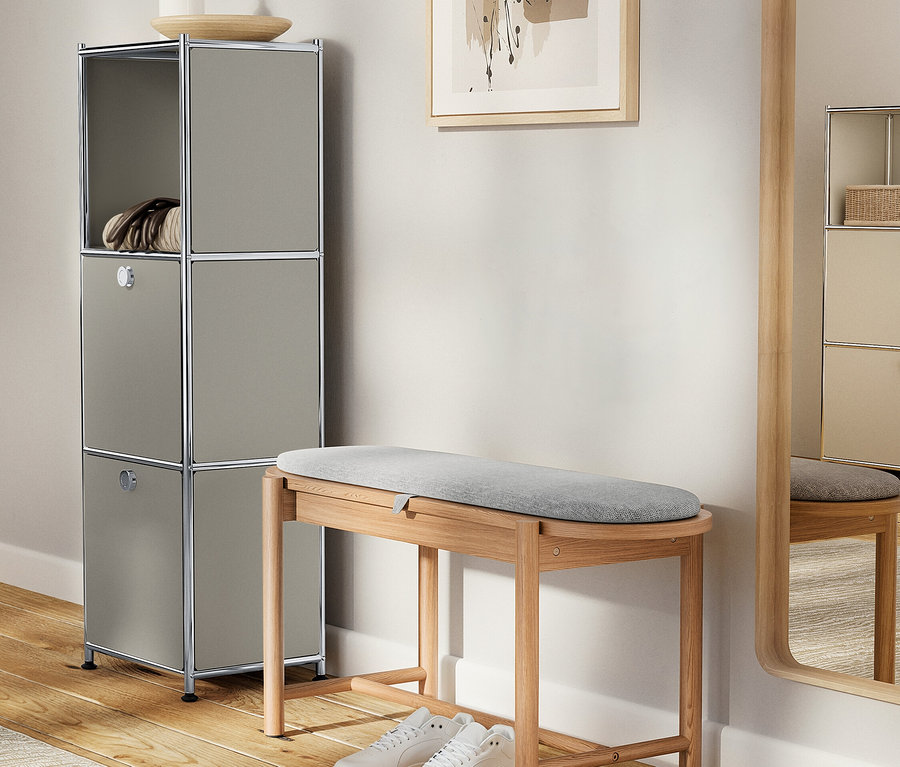 Grauer Schrank mit Dekorationen steht neben einer Holzbank mit grauer Polsterung und weißen Schuhen.