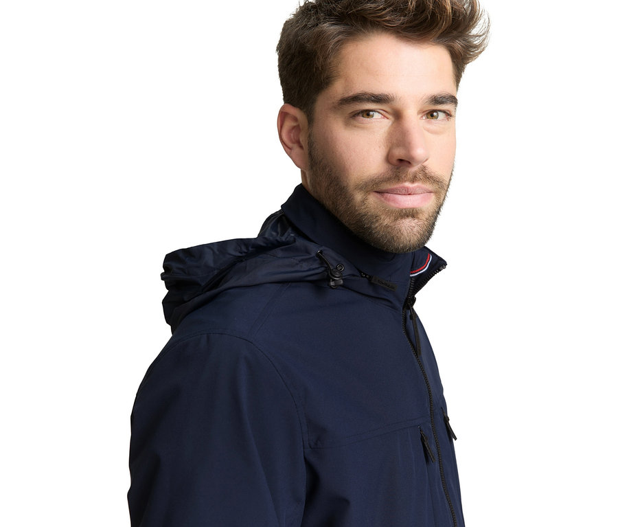 Mann trägt eine dunkelblaue Tom Tailor Blouson-Jacke, Sky Captain Blue, mit Kapuze und blickt nach vorne.