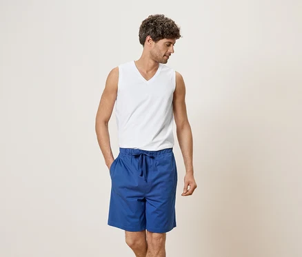 Mann mit weißem Tanktop und blauen Shorts, Hand in der Tasche.