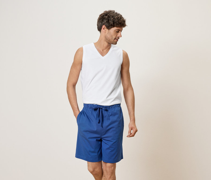 Mann mit weißem Tanktop und blauen Shorts, Hand in der Tasche.