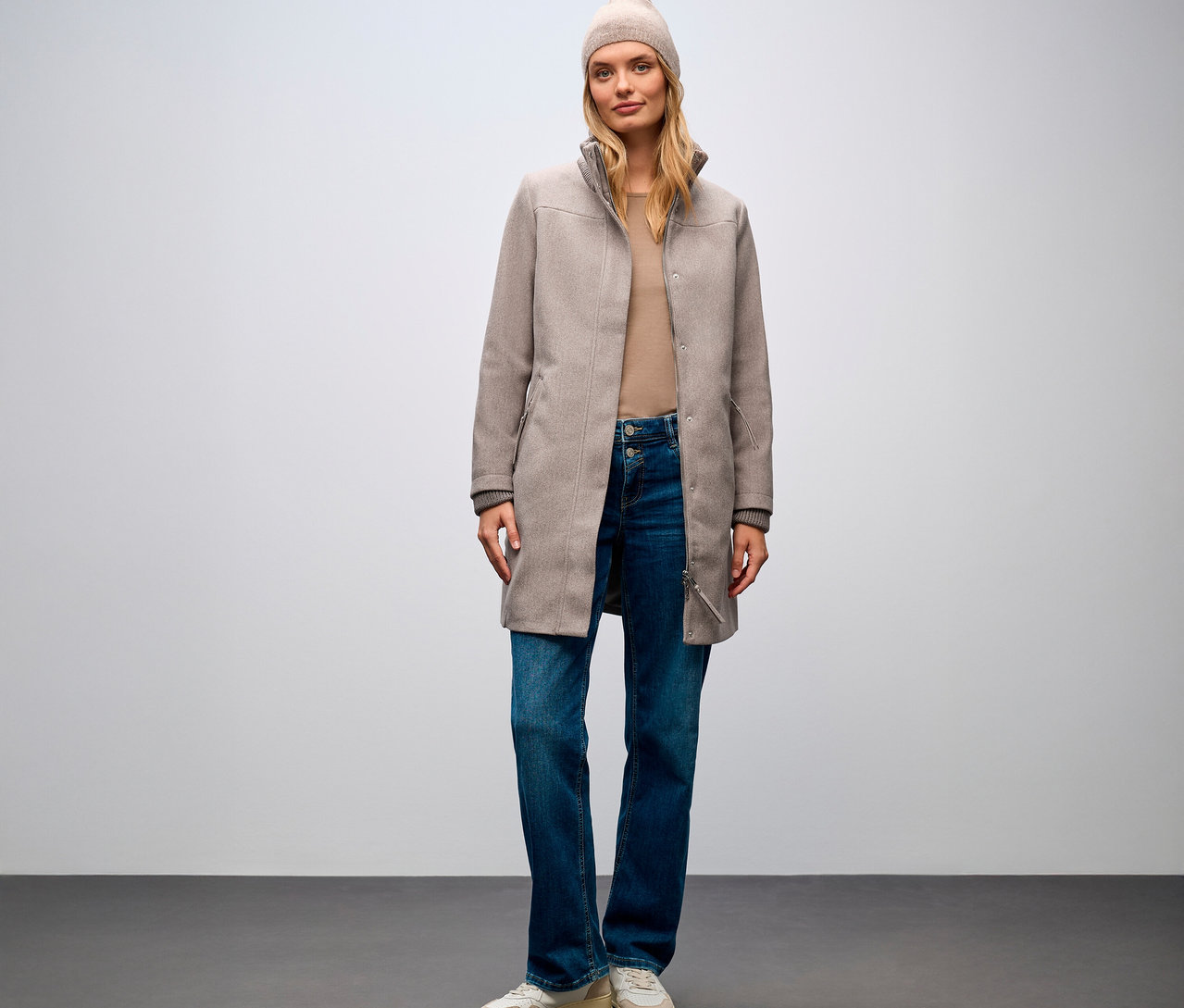 Frau steht und trägt einen Street One Kurzmantel, Jeans und eine Mütze.