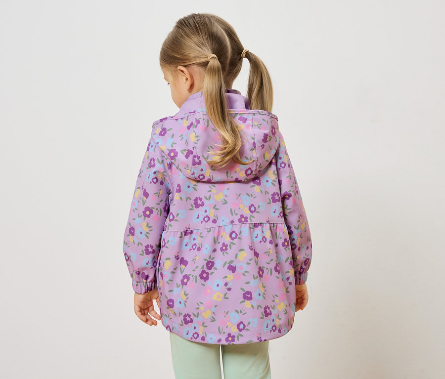 Rückansicht eines kleinen Mädchens mit blonden Zöpfen, das eine lila, geblümte Jacke und hellgrüne Hosen trägt.