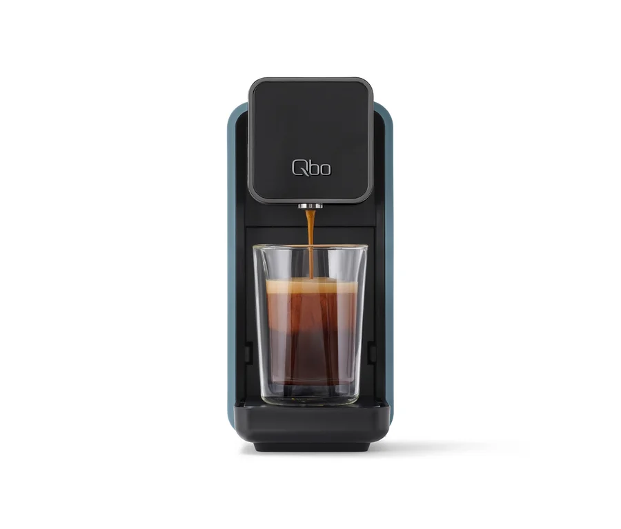 Die «Qbo ONE» Kapselmaschine in Misty Blue brüht Kaffee in ein doppelwandiges Glas.