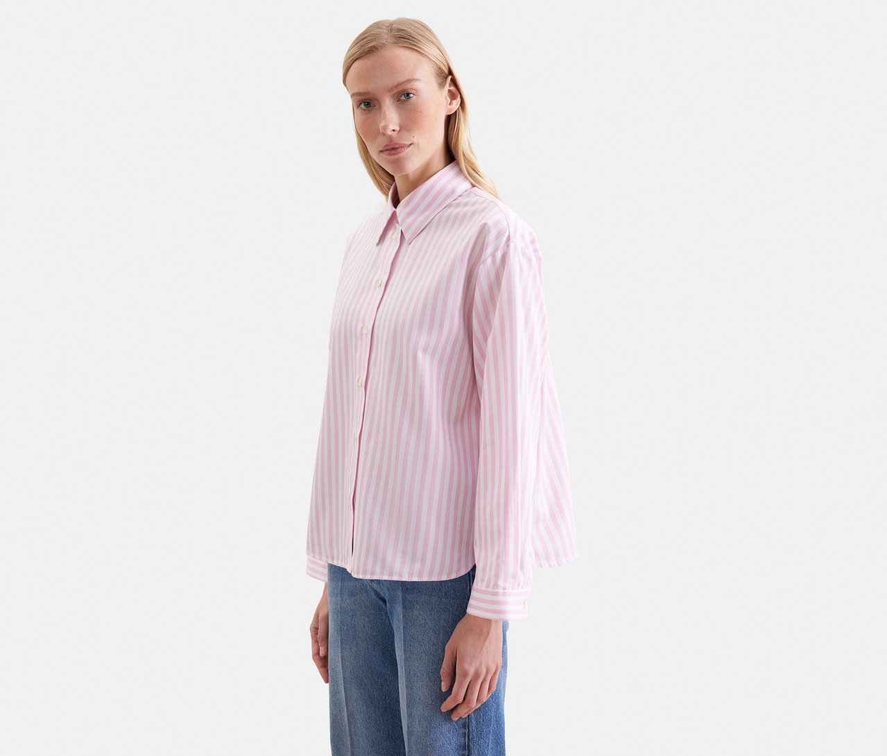 Frau trägt eine roséfarbene Seidensticker Oversize Hemdbluse mit Streifen und blaue Jeans.
