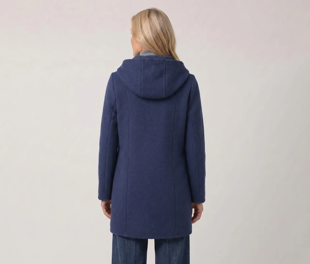 Frau von hinten in einem blauen Kapuzenmantel und blauen Jeans vor weißem Hintergrund.