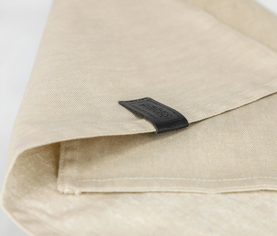 Nahaufnahme einer gefalteten, sandfarbenen Serviette der SCHÖNER WOHNEN-Kollektion mit schwarzem Etikett.