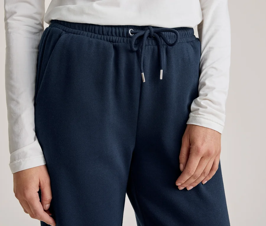 Person trägt dunkelblaue Jogginghose mit Kordelzug und weißes Langarmshirt, Hände an den Seiten sichtbar.