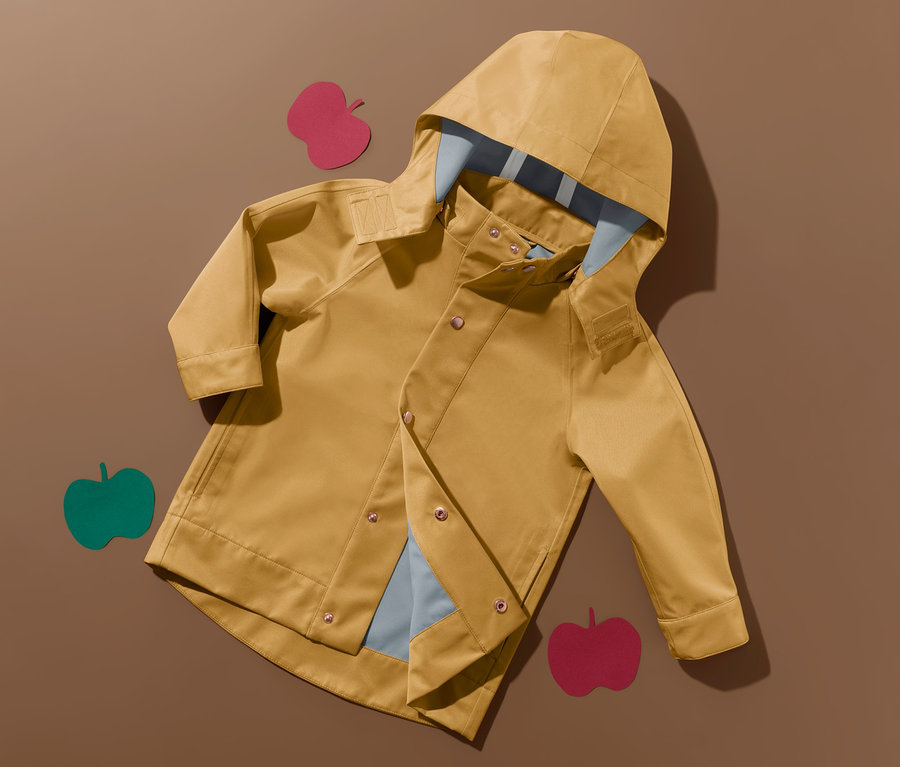 Gelbe Regenjacke aus recyceltem Material liegt offen auf braunem Grund, dekoriert mit Apfelformen.