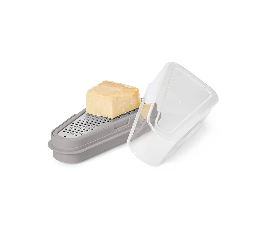 Ein Stück Käse liegt auf einer grauen Reibe mit Behälter und transparentem Deckel.
