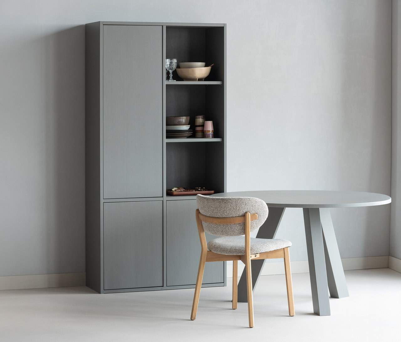 Grauer WOOOD Esstisch »Rhonda«, ca. 129 cm, mit einem Stuhl und einem grauen Schrank mit Geschirr.