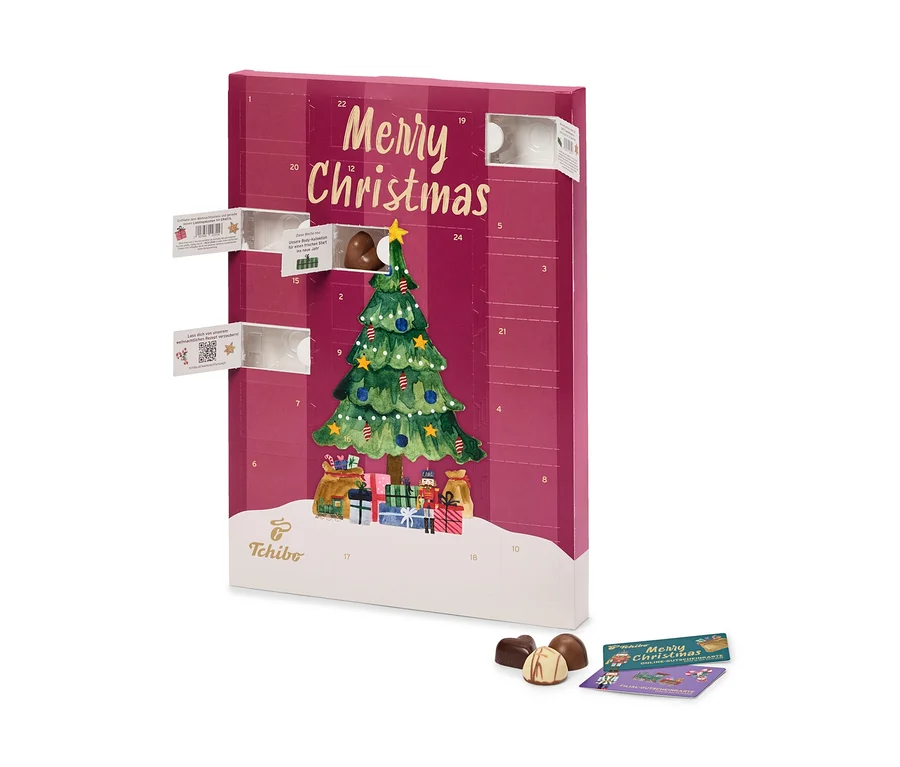 Ein aufrecht stehender roter RA AT Tchibo Adventskalender mit "Merry Christmas" und einem Weihnachtsbaum. Mehrere Türchen sind offen, eines zeigt eine Praline. Drei Pralinen und zwei Karten liegen davor.