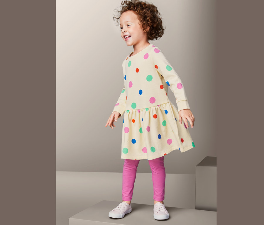 Lächelndes Mädchen im Sweatkleid mit bunten Punkten.